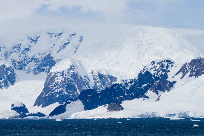 The mountains have no trees or any other feature to judge their size. Here you can see a boat  below the mountain, and suddenly the size becomes apparent. It's possible to see similar height mountains all over the world, but not with that much snow, and not that much snow right down to sea level. Maybe in Greenland, but I've never visited Greenland.